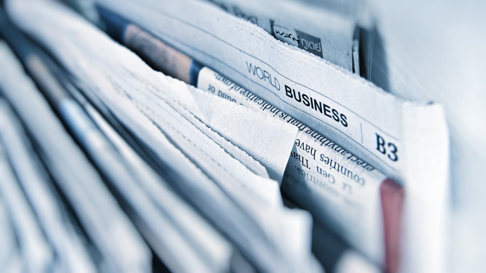 A close-up stack of folded newspapers open at the business pages